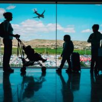 Photo of a family with kid at an airport, looking out the window at a plane.