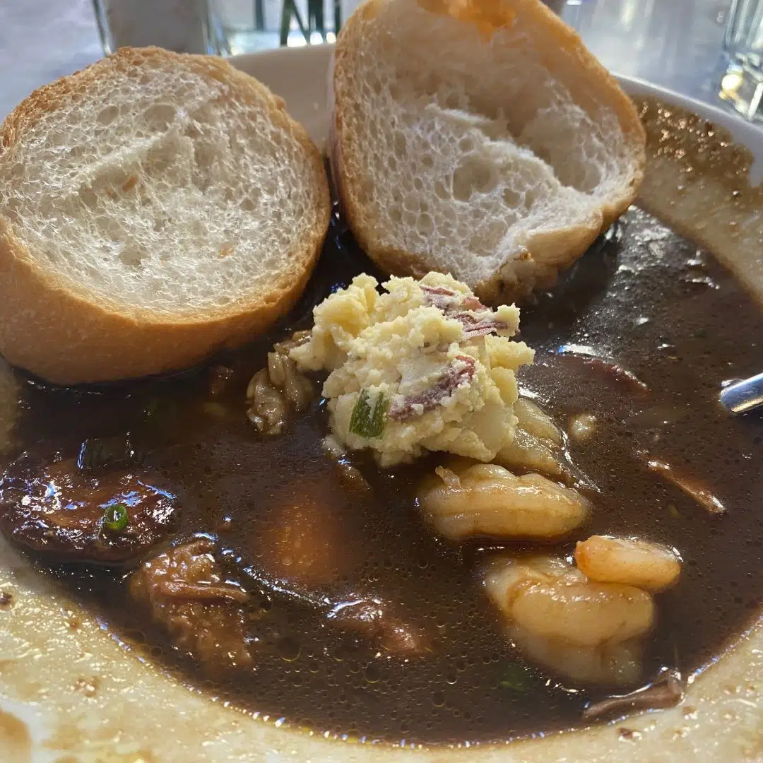 Closeup of a bowl of New Orleans gumbo with potato salad and bread on the side.