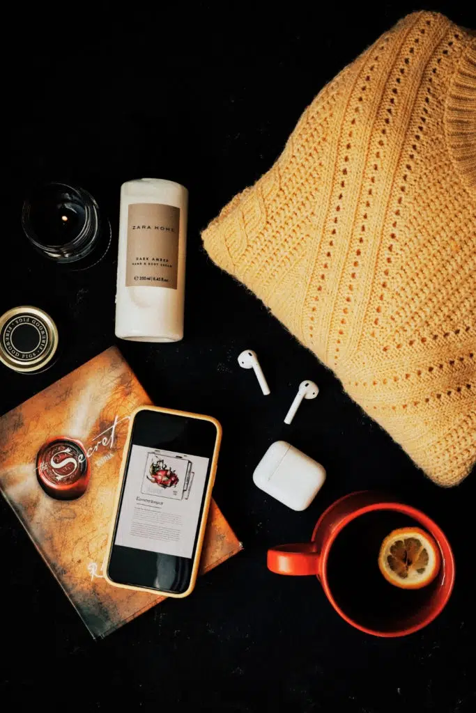Flat lay photo with a candle, sweater, mug of tea, and a copy of the book "The Secret," by Rhonda Byrne.