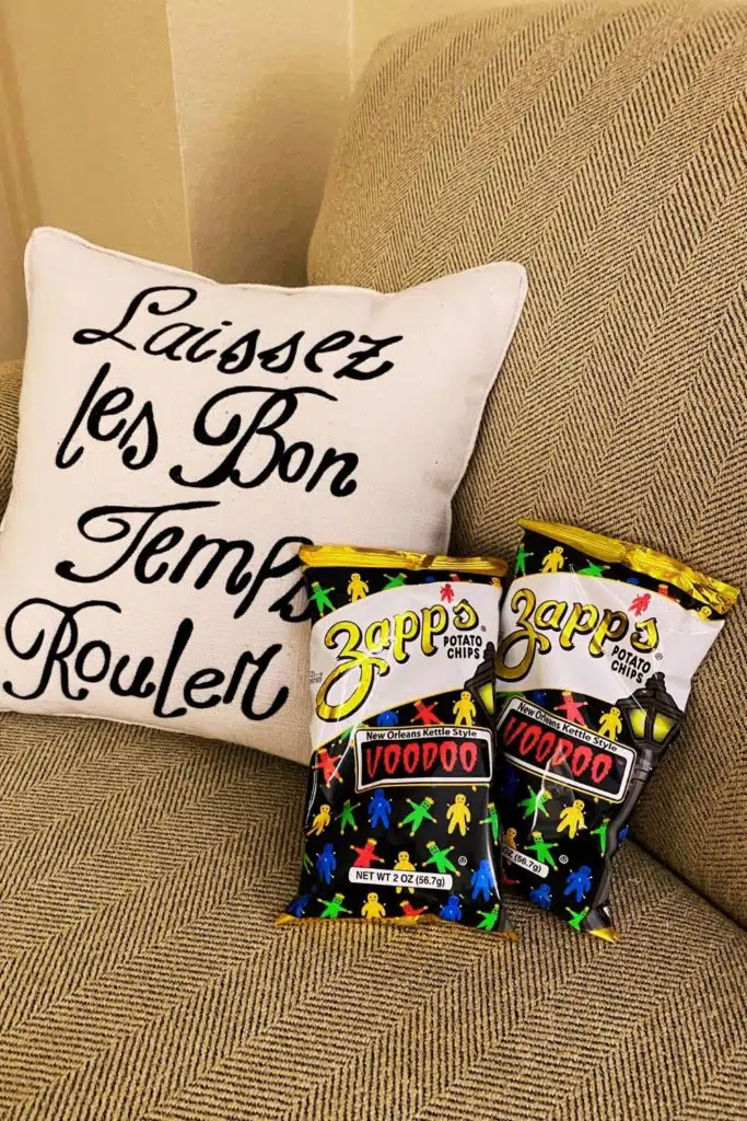 Photo of 2 large bags of Zapp's Voodoo potato chips sitting on a couch next to a pillow that says "Laissez les bon temps rouler."