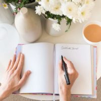 Photo of a notebook open to a blank page with a person posed to start writing.