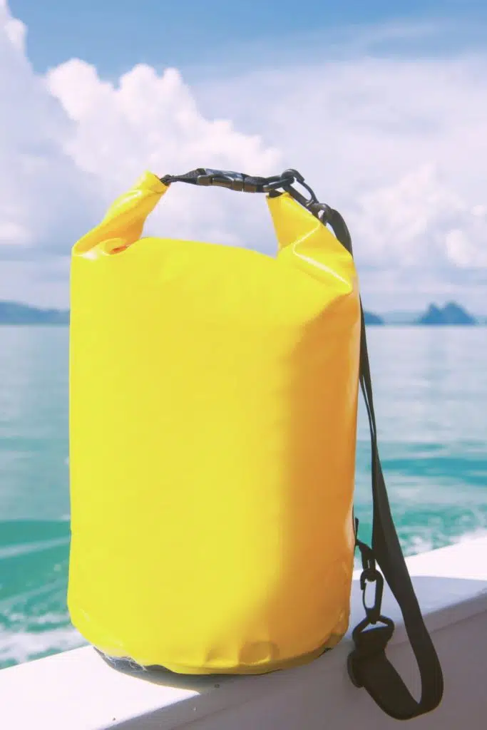 Closeup of a bright yellow dry bag sitting on the edge of a boat with the ocean in the background.