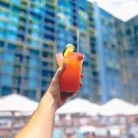 Photo of a person holding up a cocktail while relaxing poolside.