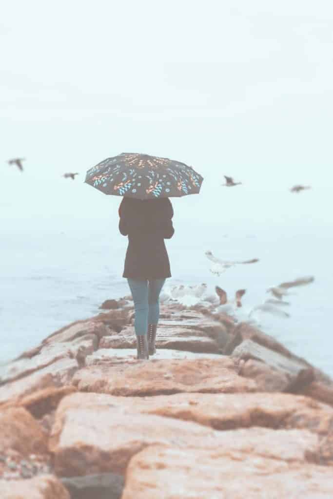 Phooto of a woman walking down a rock path with an umbrella up.