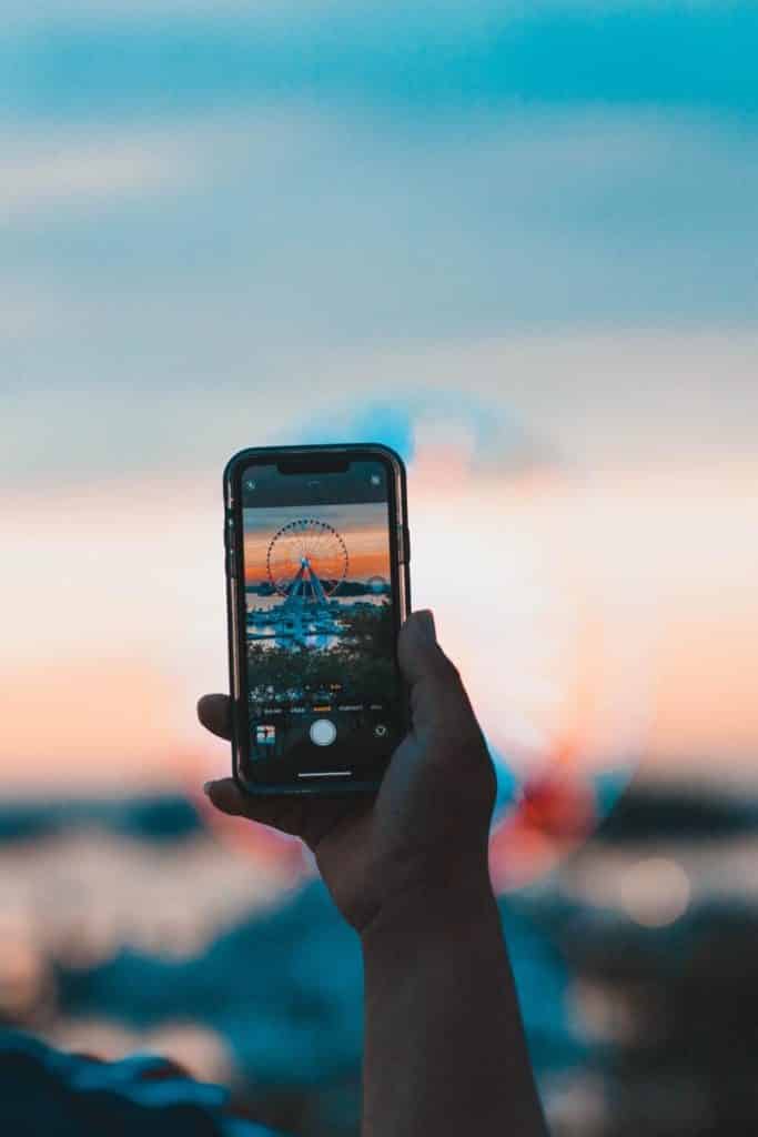 Photo of a person holding up a phone open to a photo of a ferris wheel.