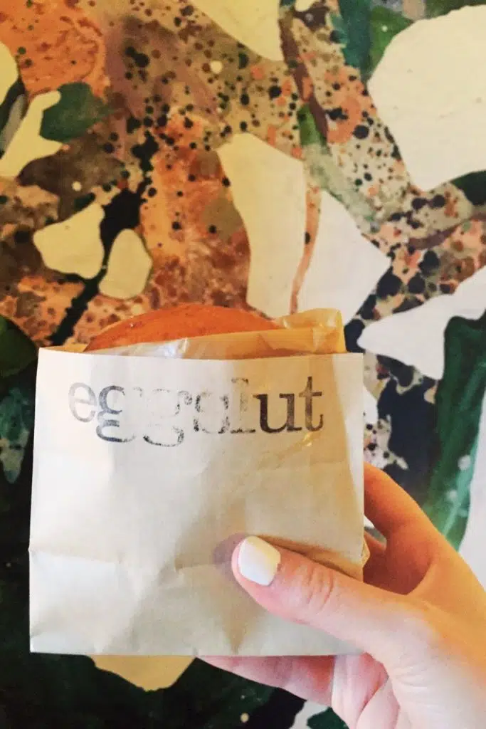 Closeup of a person holding an egg sandwich in a paper wrapper that says "Eggslut."
