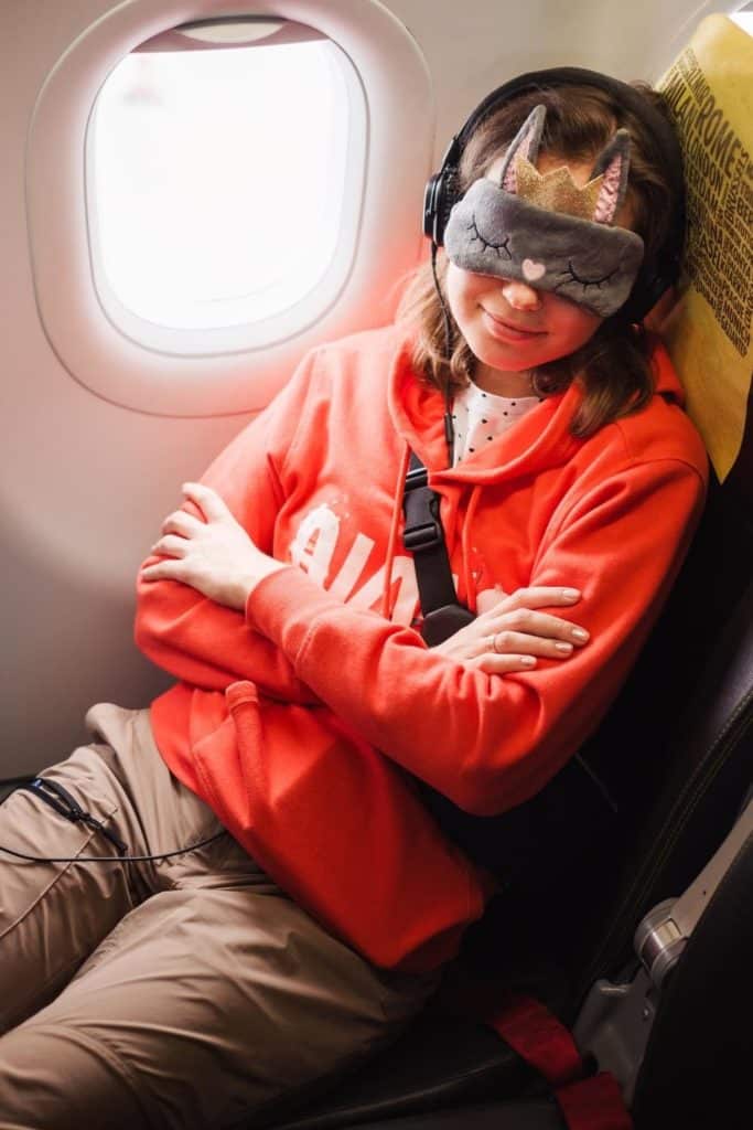 Photo of a young person napping on a plane with a sleep mask and headphones on.