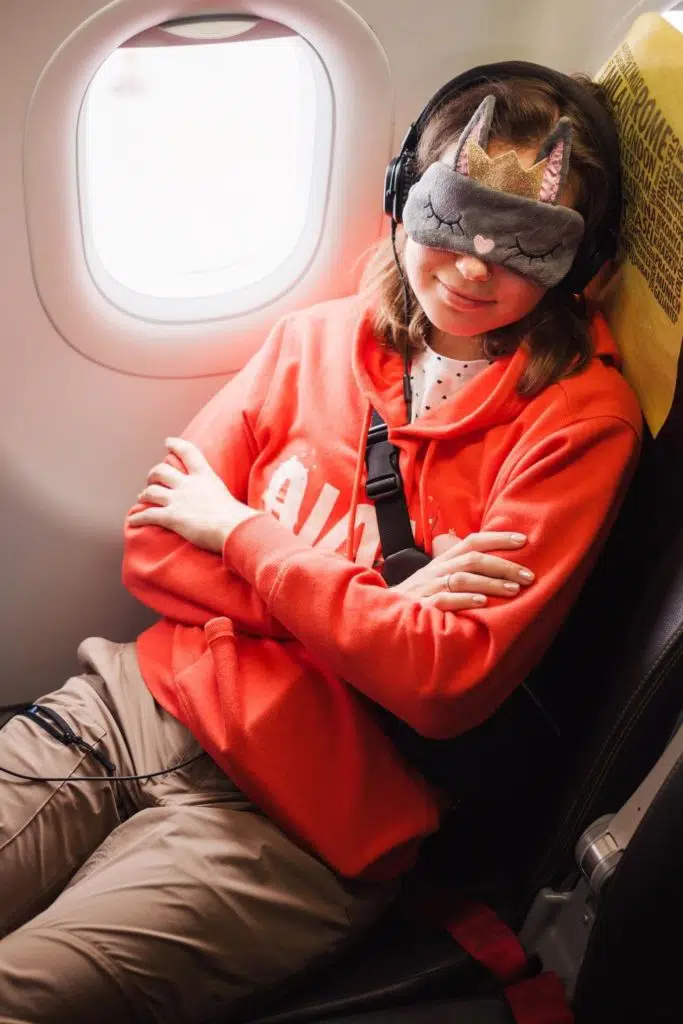 Photo of a young person napping on a plane with a sleep mask and headphones on.