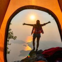 Photo from inside a tent with a woman standing on a ledge overlooking a lake.