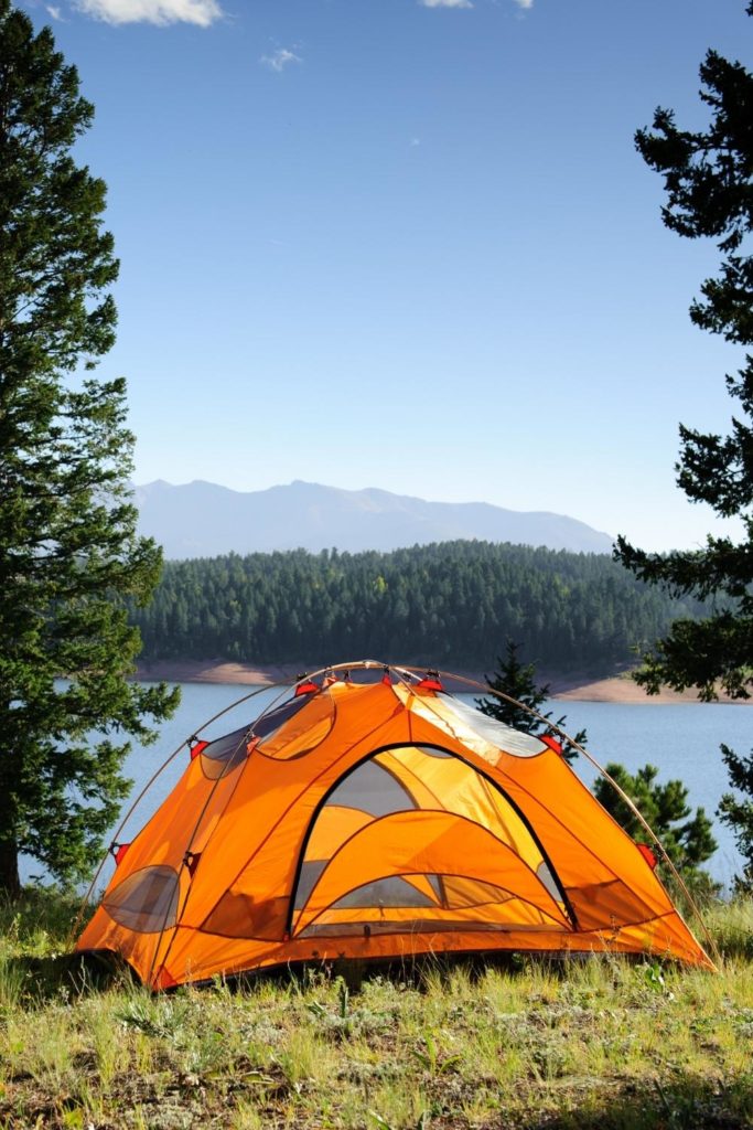 Photo of an empty bright orange tent with a lake in the background.