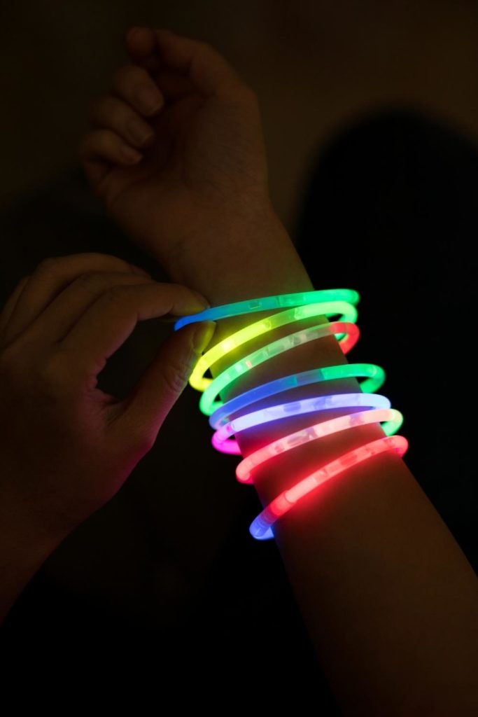 Closeup of a person wearing a stack of glow stick bracelets in the dark.