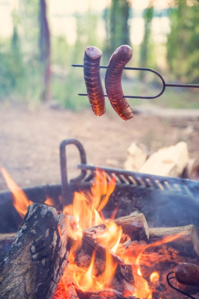 Closeup of 2 hot dogs cooking over a campfire.