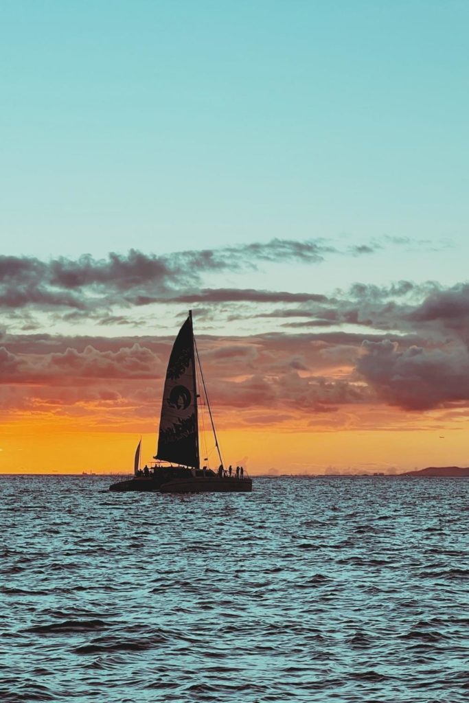 Photo of a catamaran sailing during sunset.