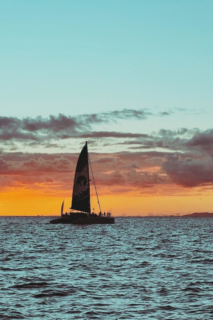 Photo of a catamaran sailing during sunset.