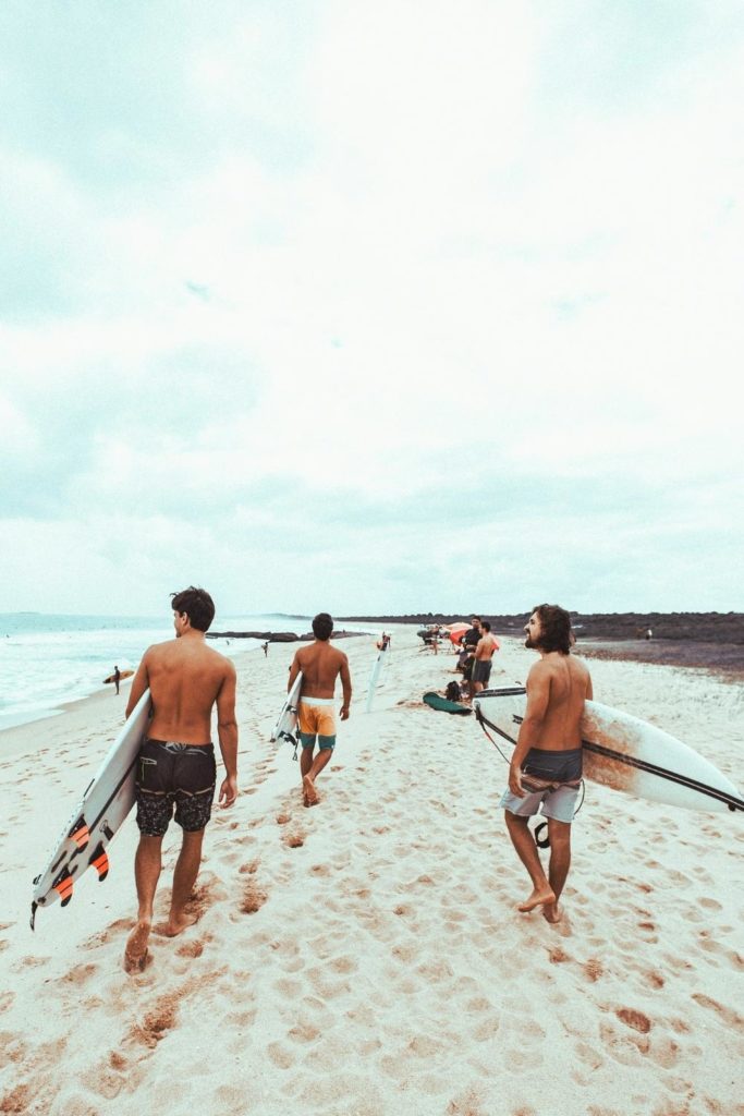 Photo of a group of men holding surfboards, walking on the beach.