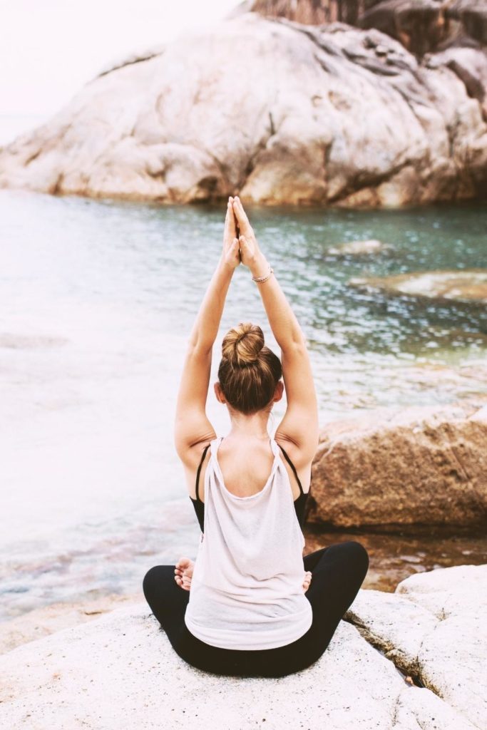 Photo of a woman doing a sitting yoga pose on a rock in front of the ocean.