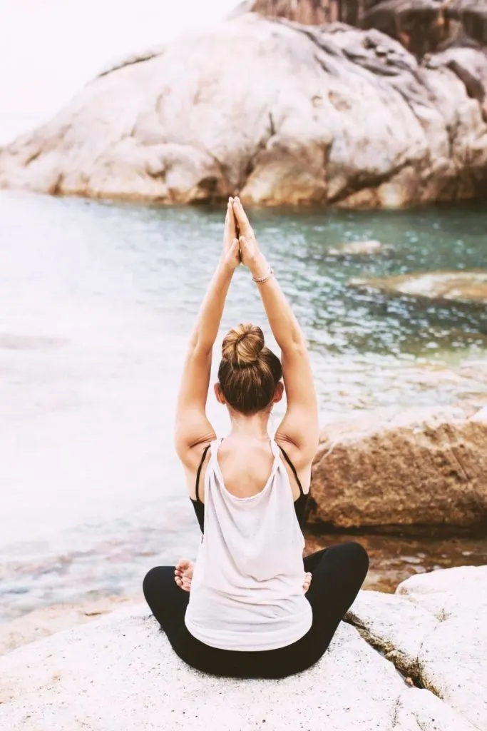 Photo of a woman doing a sitting yoga pose on a rock in front of the ocean.