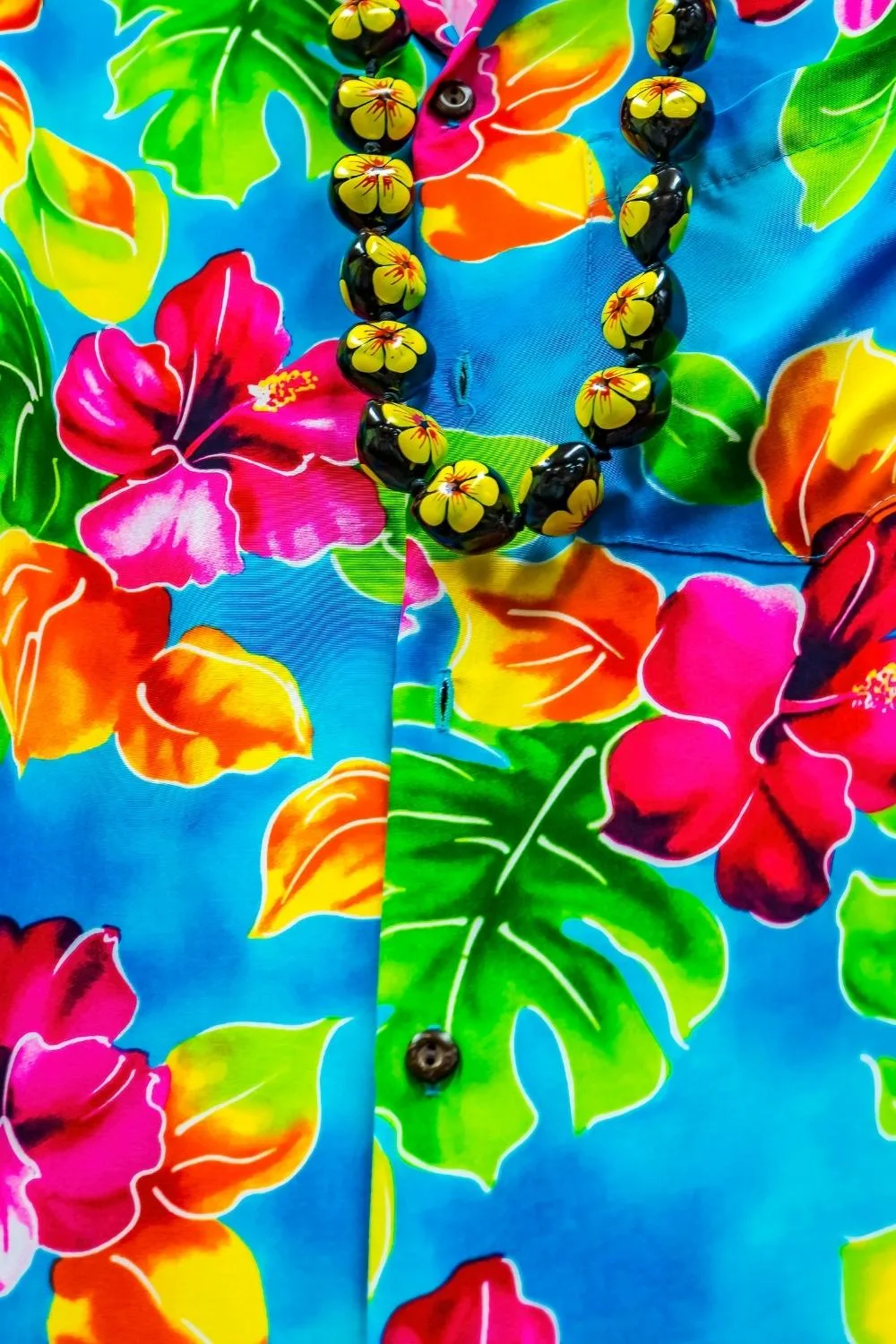 Closeup of a bright blue Hawaiian shirt and kukui nut lei.