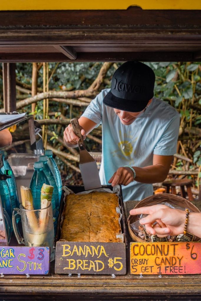 Phot of a man cutting a slice of banana bread at a roadside stand in Maui.