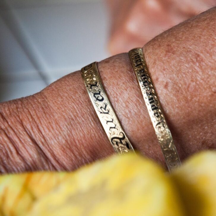 Closeup of a woman wearing 2 gold bracelets in the Hawaiian Heirloom style.