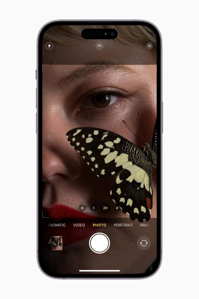 Photo of the iPhone 14 Pro with the camera mode open while taking a photo of a woman with a butterfly on her cheek.