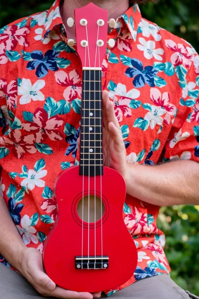 Closeup of a man wearing a Hawaiian print shirt while holding a red ukulele.