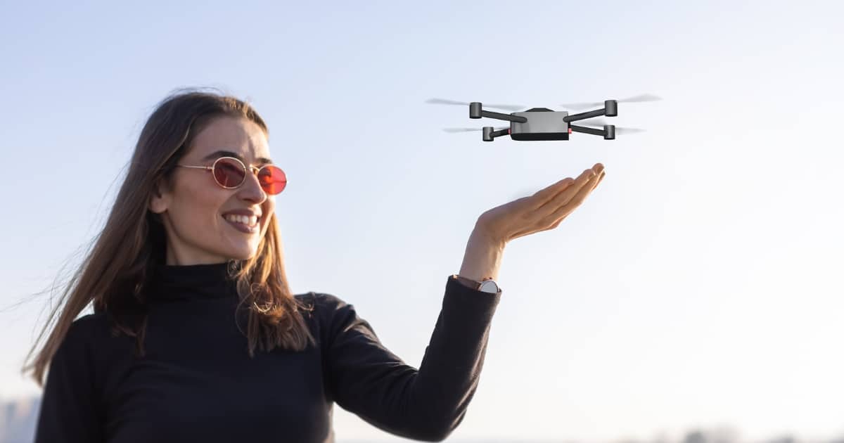 Photo of a woman with her hand stretched out with a small drone hovering above it.