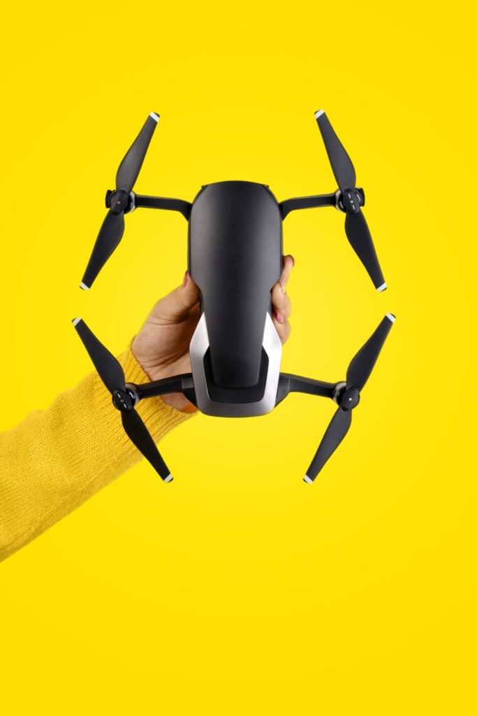 Photo of a compact drone for beginners held against a yellow background.