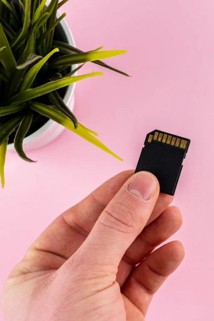 Closeup of a camera memory card held against a pink background.