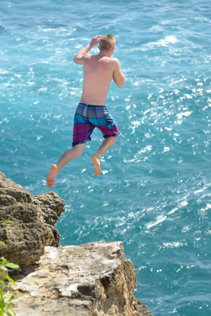 Photo of a boy jumping off a cliff into an ocean.