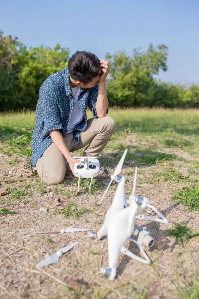 Photo of a man crouched on the ground behind a crashed drone.