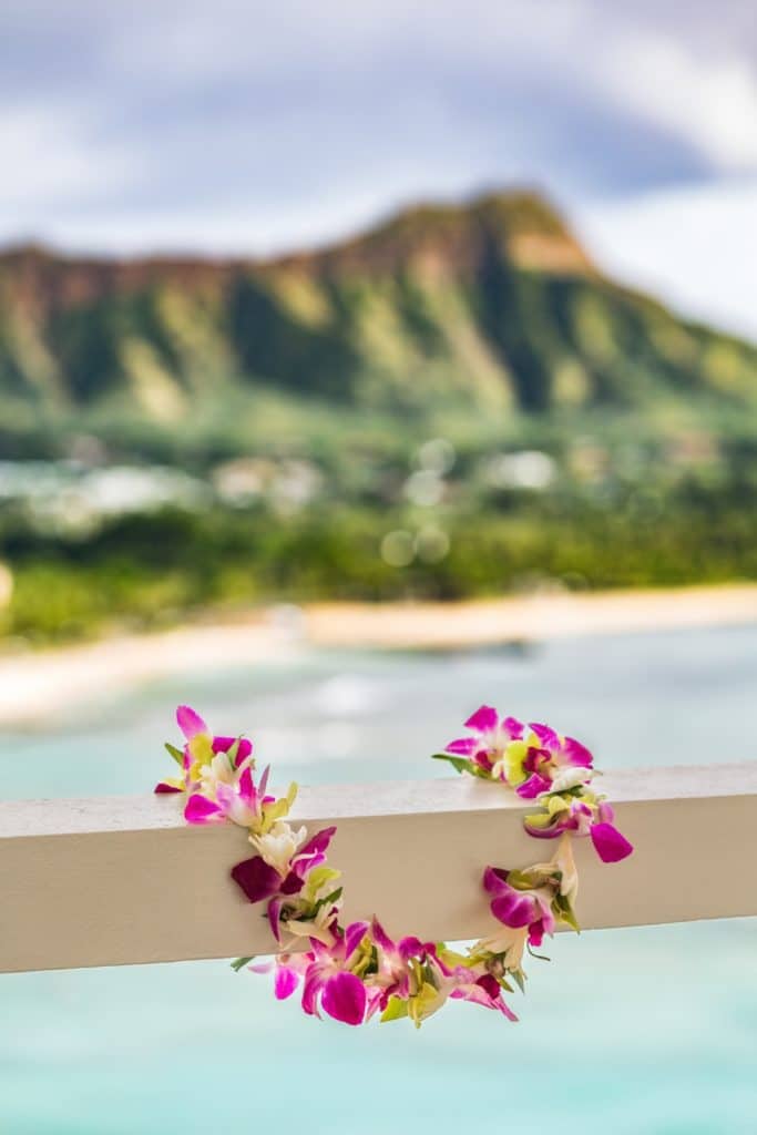 Photo of a real Hawaiian lei draped over a balcony rail with Diamond Head in the background.