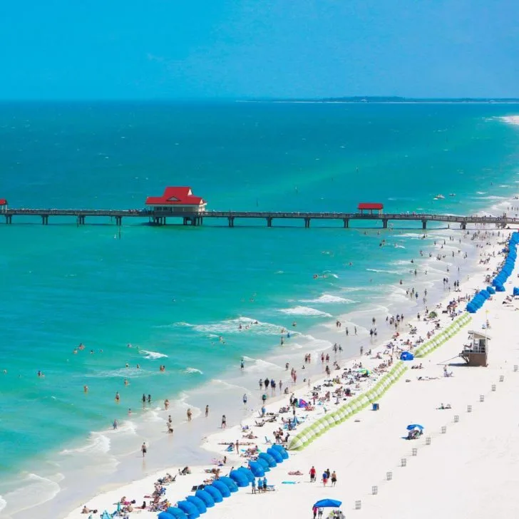 Aerial photo of Clearwater Beach in Florida with the sand packed with people and beach huts and a boardwalk in the background.