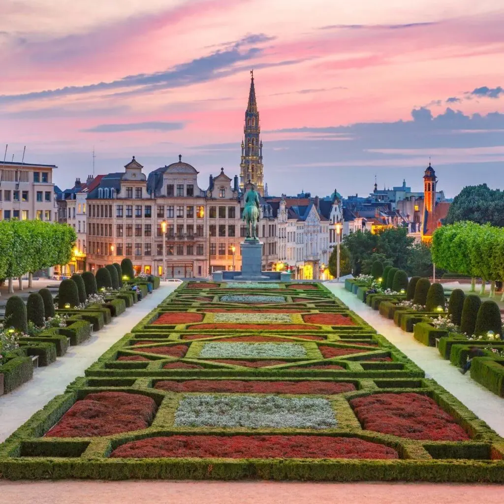 Photo of old town Brussels in Belgium during sunset with an elaborate garden in the foreground and ornate buildings in the background.