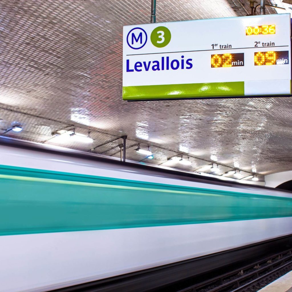 Photo of train signage in a station in Paris France while a train speeds by.