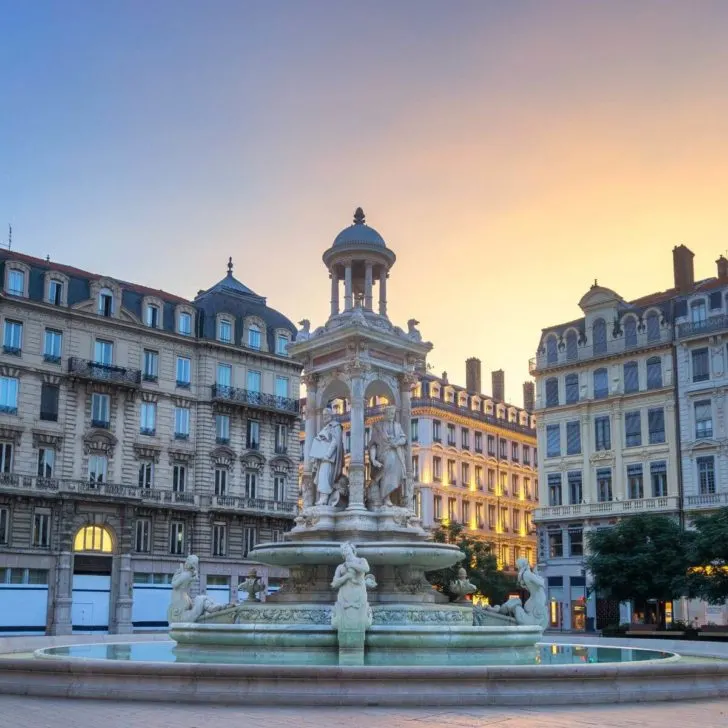 Photo of a public square in Lyon, France with ornate buildings and a statue in a fountain.
