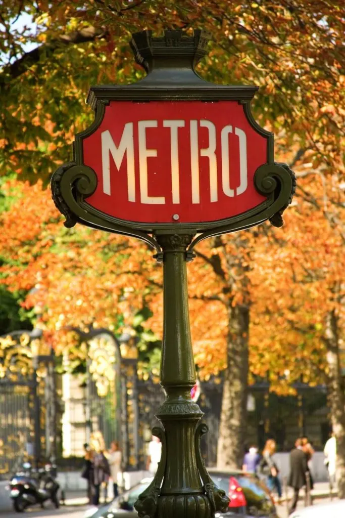 Photo of a red metro station sign in Paris with orange Autumn leaves in the background.