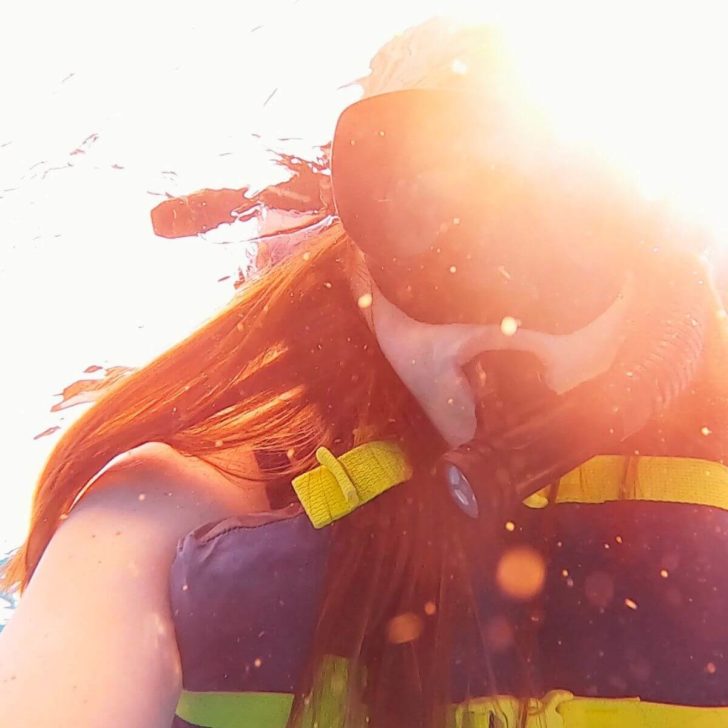 Closeup of a woman wearing a snorkel mask and vest underwater.