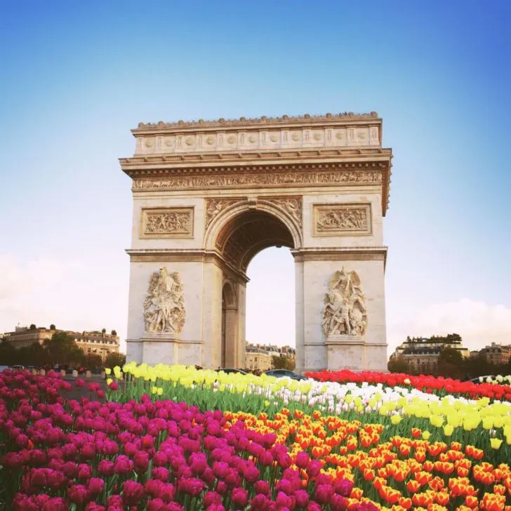 Photo of the Arc de Triomphe in Paris with tons of tulips planted in the foreground.