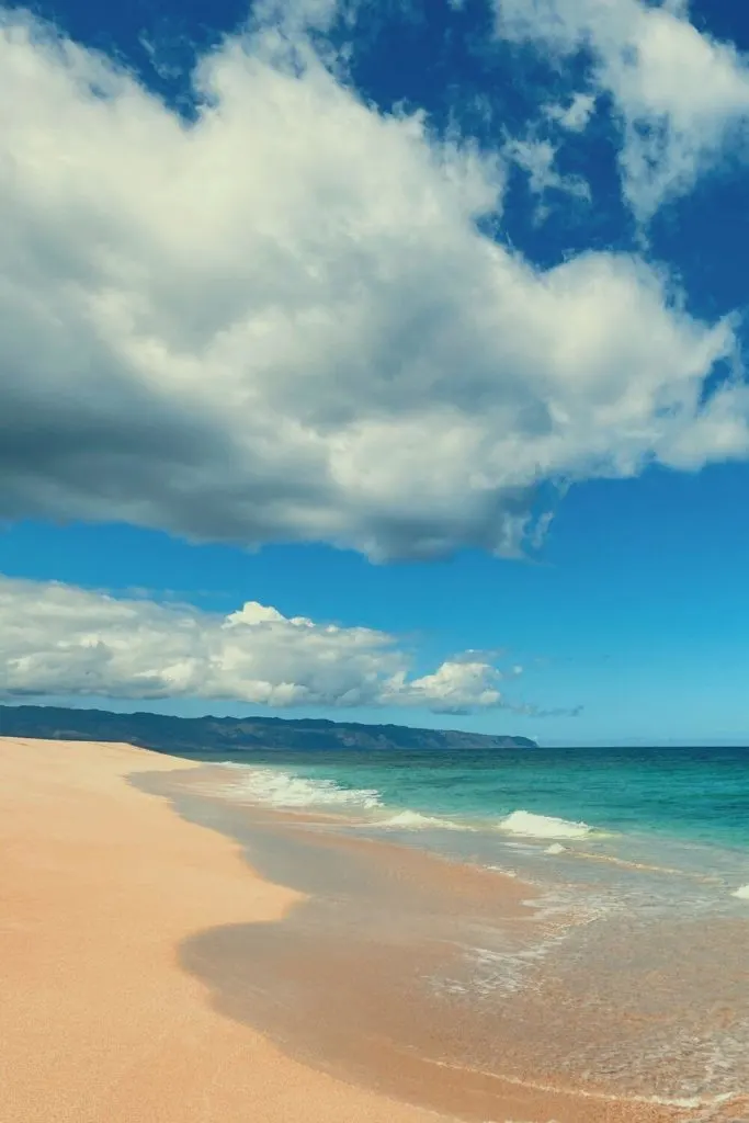 Photo of a pristine beach with peachy colored sand and turquoise waters.