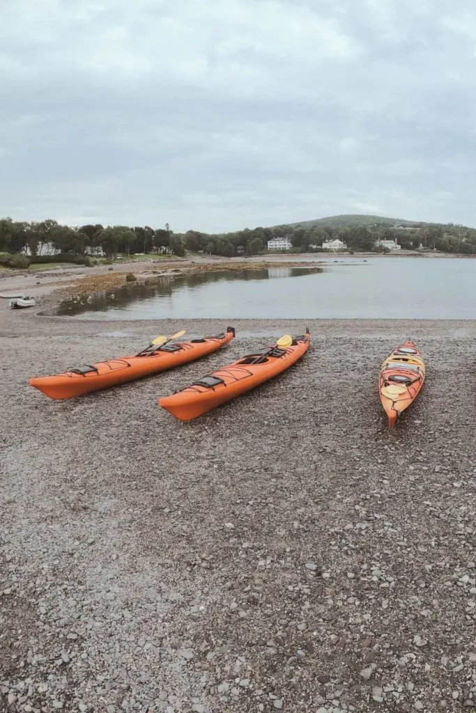Photo of 3 orange kayaks lined up along the gravel sand bar path to Bar Island in Acadia National Park.