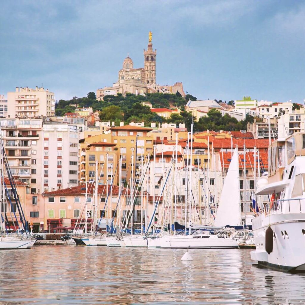 Photo of the Basilique Notre-Dame de la Garde from the marina below it with boats in the foreground.