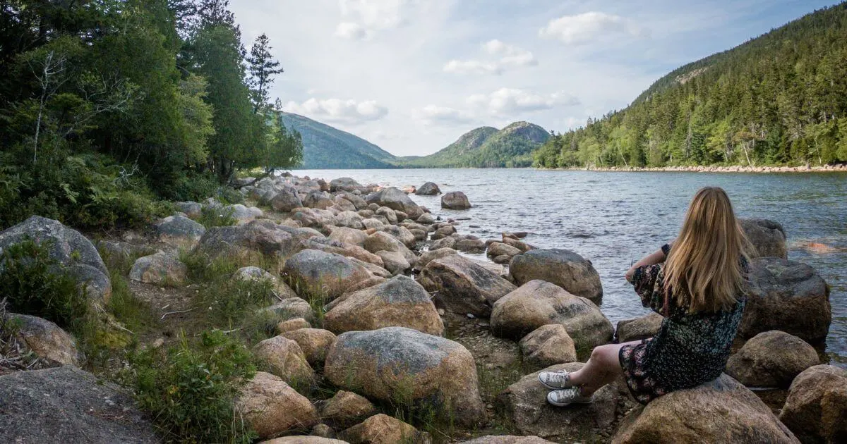 Photo of a woman sitting on a large rock along Jordan Pond Path in Acadia National Park in Maine.