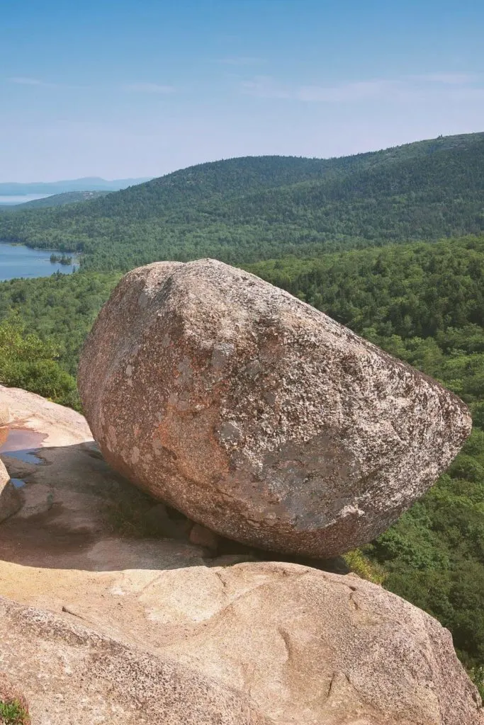 Photo of Bubble Rock in Acadia National Park with lots of lush green trees in the background.