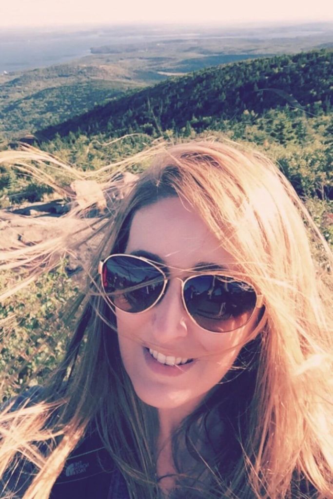 Photo of a woman at the Cadillac Mountain summit with the wind blowing in her hair.