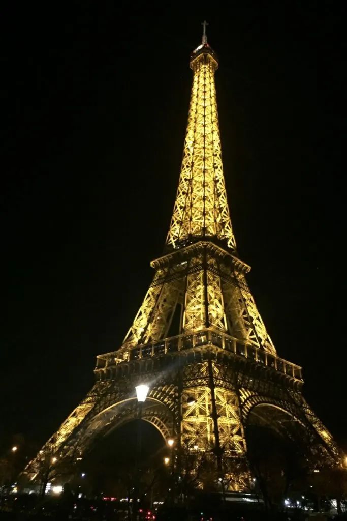 Photo of the Eiffel Tower at night, light up in yellow lights.