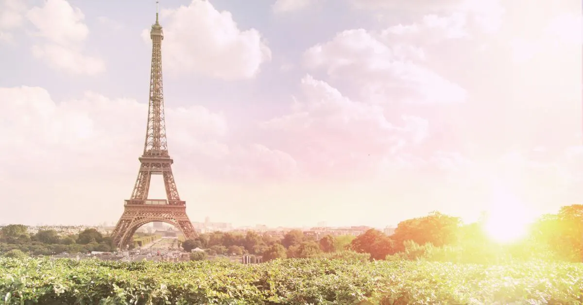 Photo of the Eiffel Tower in the background with greenery in the foreground and the sun setting in the corner.