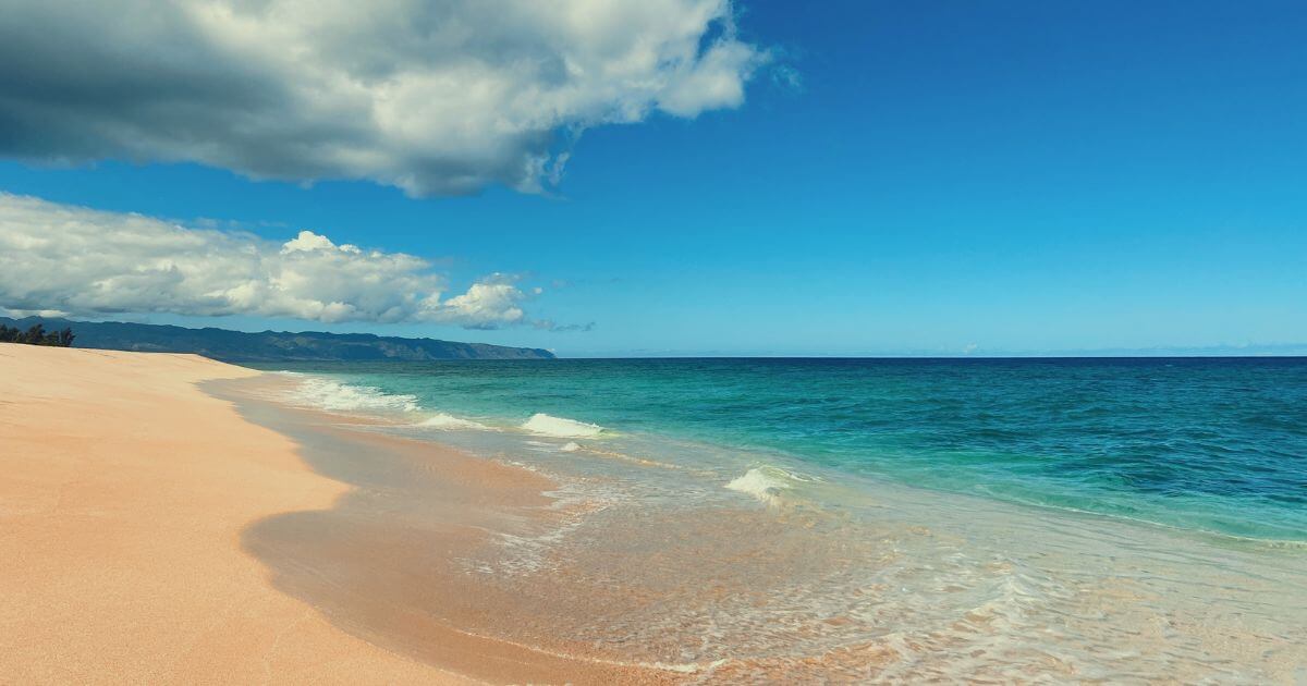 Photo of 'Ehukai Beach Park on the north shore of Oahu with calm surf, pristine sand, and no people.