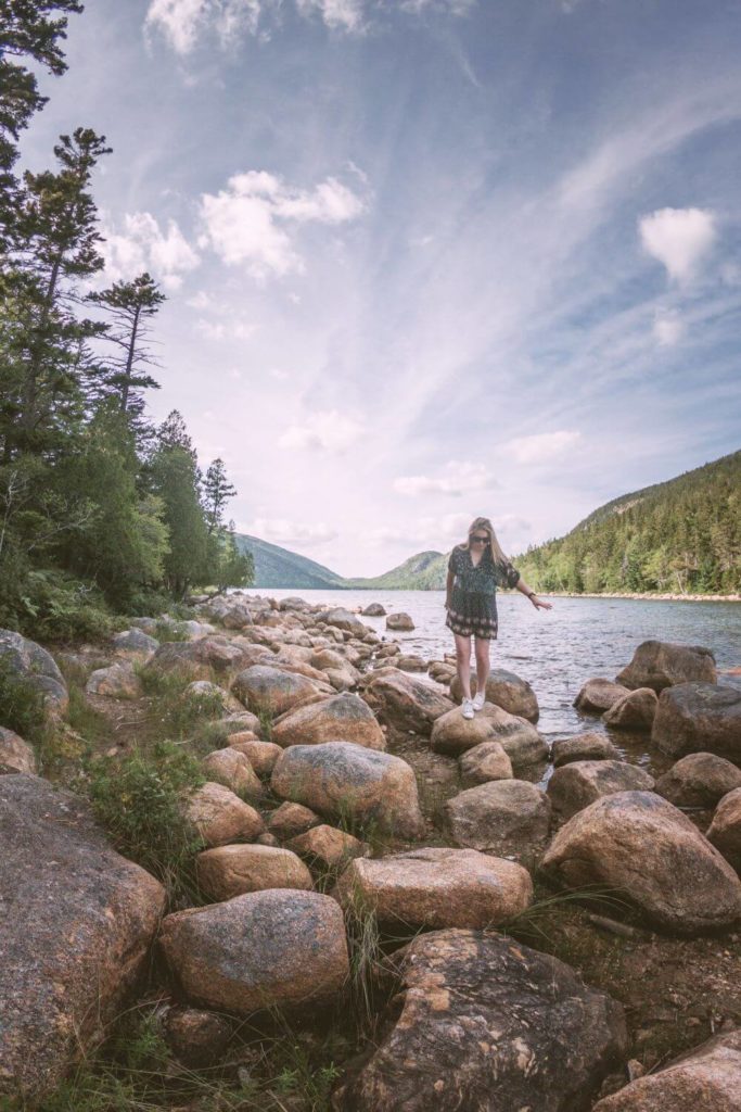 Photo of a woman walking across large rocks along Jordan Pond.