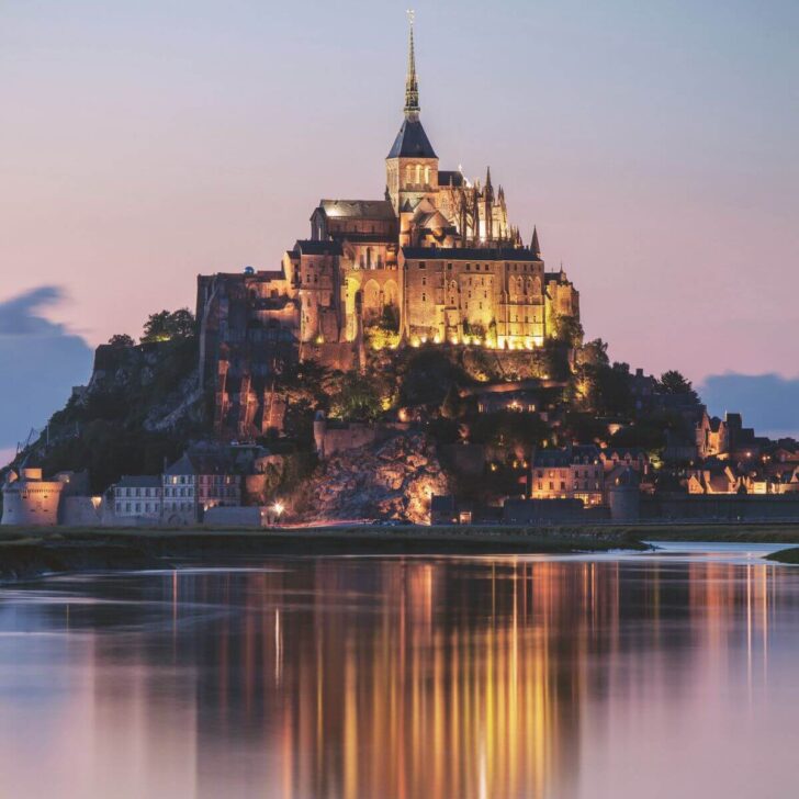Photo of Mont Saint-Michel at dusk, reflecting in the wet sand below it.